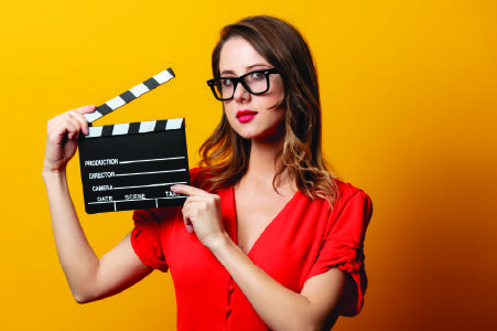 A girl holding a movie clapper board on a yelloe background